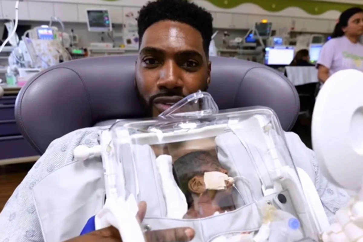 Foto colorida de homem segurando um bebê prematuro através de uma incubadora móvel - Metrópoles.